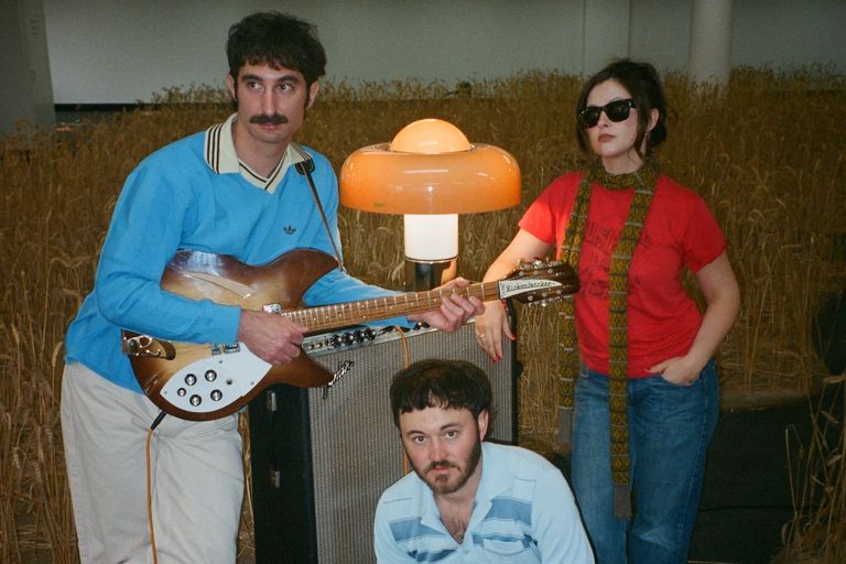 Indie pop band San Cisco posing with a guitar, amp, and retro mushroom lamp in a field, photo by Mitchell Benson.